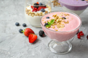 Different tasty yogurts with fresh berries and granola in glass dessert bowls on gray textured table, closeup