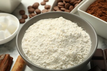 Flour in bowl and chocolate for making dough on white table, closeup