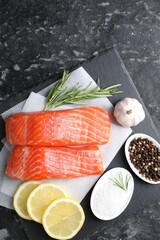 Pieces of fresh salmon with rosemary, lemon, garlic and spices on dark textured table, top view
