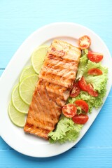 Delicious grilled salmon fillet with vegetable salad and lime on light blue wooden table, top view