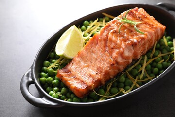 Delicious grilled salmon fillet with green peas and lime in baking dish on grey table, closeup