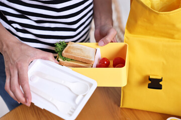 Woman packing lunch box at wooden table in kitchen, closeup. Preparing for school