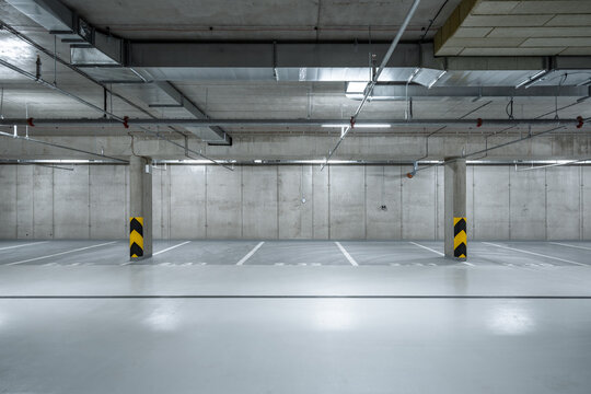 A well-lit underground parking garage with empty parking spaces, concrete columns, and visible overhead pipes, exuding an industrial atmosphere.