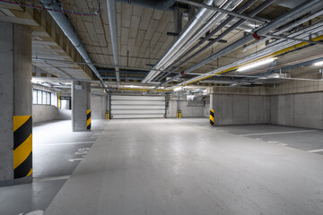 A spacious underground parking garage with exposed pipes on the ceiling, yellow and black striped...