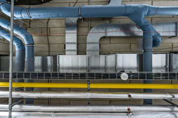 A complex arrangement of blue insulated pipes, metal ducts, and cables in an industrial setting, possibly for ventilation or gas systems in a factory or power plant.