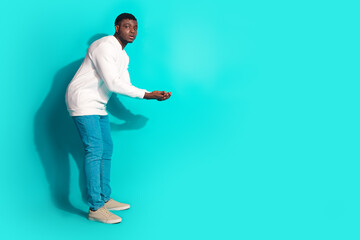 Naklejka premium Full body photo of attractive young man hold empty space dressed stylish white clothes isolated on cyan color background