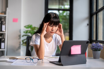 Young asian businesswoman having headache while working on digital tablet at office