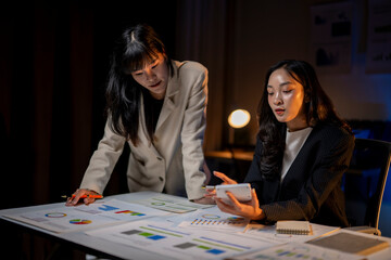 Fototapeta premium Two businesswomen working late analyzing financial charts and using calculator