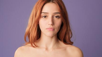Fototapeta premium Close-up of red-haired woman looking at camera on purple background. Beautiful girl poses in studio with blank space on violet wall for your promotion