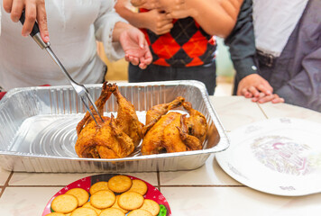 A family gathers around a roasted chicken being served on a metal tray. The close-up image captures the warmth of a home-cooked meal and the joy of togetherness during a festive occasion. 