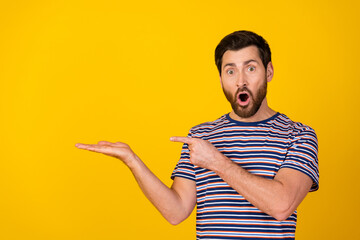 Fototapeta premium Photo of speechless man dressed striped t-shirt directing at palm presenting product empty space isolated on yellow color background