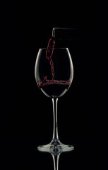 Red wine is poured into a glass from a bottle, forming beautiful bubbles.