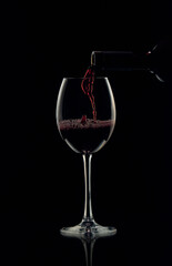 Red wine is poured into a glass from a bottle, forming beautiful bubbles.
