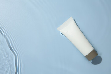 Cosmetic product. Tube with cream in water on light blue background, top view. Space for text