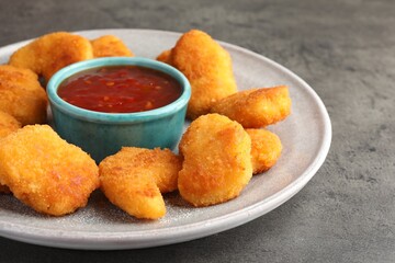 Plate with hot chili sauce and nuggets on grey textured table, closeup
