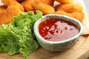 Hot chili sauce, lettuce and nuggets on wooden board, closeup