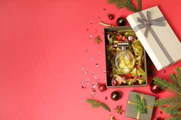 Perfume bottle in gift box and Christmas decor on red background, flat lay. Space for text