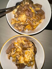 Two plates of scrambled eggs and meat, one above the other, on a dark table with a fork resting nearby.