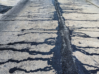 Asphalt on road. Street with black tar filling the cracks. Cracks in concrete surface are then...