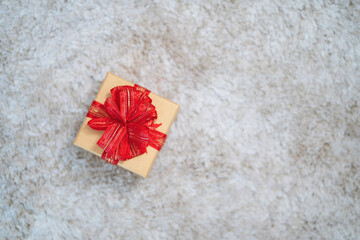 A small brown box with a red bow on top of it. The box is sitting on a white carpet