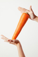 Person holding an orange carrot in one hand with the other hand on the opposite side