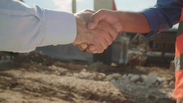 Close-up of hands of man in yellow vest and man in white shirt shaking hands on blurred background of construction site. Deal concept. Business. Geodesy. Outdoors