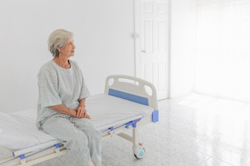 Obraz premium Elderly patient woman sitting on a hospital bed. The image conveys a sense of solitude and contemplation, as the patient appears to be reflecting during her stay in the healthcare facility.