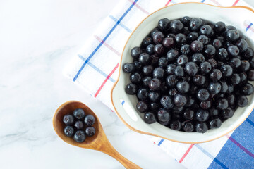 Ripe chokeberries (aronia) in a bowl on white kitchen table. Top view.