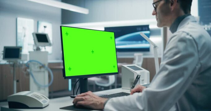 A Male Scientist in a White Lab Coat Analyzes Data on a Green Screen Computer in a Advanced Medical Lab, Focusing on Advanced Healthcare Research and Technology in a High-tech Hospital Environment.
