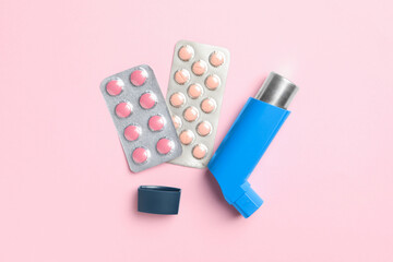 Asthma inhaler and pills on pink background, flat lay