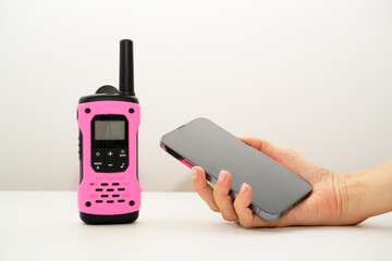 Means of communication. Pink walkie-talkie on a white table and mobile phone in a woman’s hand