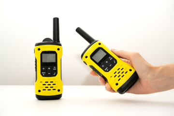 Two yellow walkie-talkie. One stands on the table the other in a woman&rsquo;s hand on a white background. Means of communication 