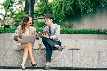 A male and female business team engage in discussion utilizing a laptop and notes. team sitting at outdoor pedestrian landscape. reflecting the importance of collaboration and strategic planning.