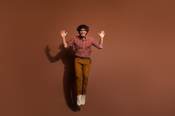Full size photo of nice young man jump rejoice wear striped shirt isolated on brown color background