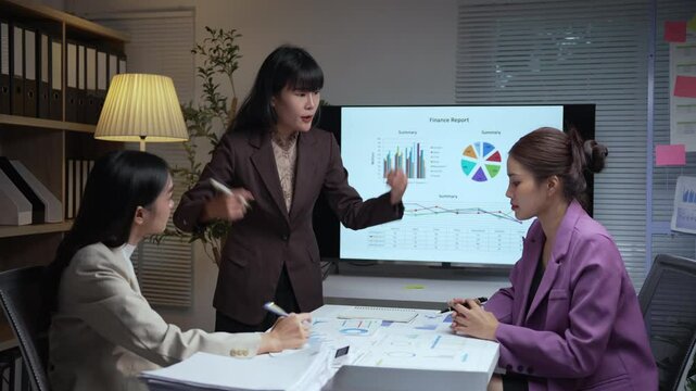Three businesswomen analyzing financial reports in a well lit office at night. Tension fills the air as they debate strategies, with one expressing visible frustration