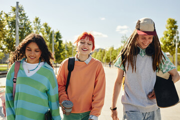 Candid shot of three smiling multiethnic teenagers in bright clothes walking together in park after...