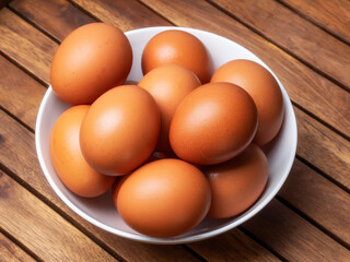 Huevos morenos de gallina en un bol sobre mesa de madera