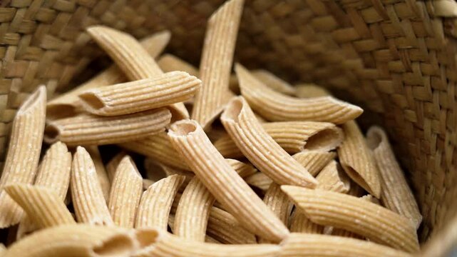 Dry quinoa penne pasta for a wholesome meal. Organic gluten free macaroni falling in slow motion into a wicker rustic bowl. Healthy food raw ingredients