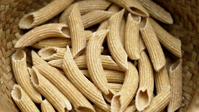Uncooked penne quinoa pasta with textured shape. Unique raw natural ingredients for gluten free diet in a rustic basket. Rotation