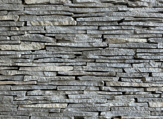 Striped cut combed andesite stone wall cladding stacked on one another. Andesite stone or lavastone for outdoor architectural wall finishing, in grey color. Seamless texture