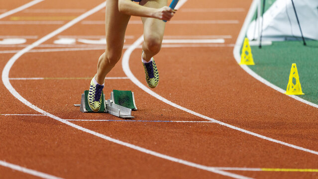 Athlete in sprinting shoes launches off the starting blocks during a competitive track race on an indoor arena surface
