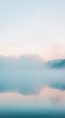 Serene landscape featuring misty mountains and calm water reflecting soft morning light.