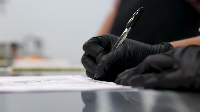 a cook in black gloves in the kitchen writes down a recipe with a black pen in a notebook