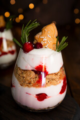A glass of Christmas dessert with gingerbread cookies, whipped cream and cranberries on dark wooden background - photo with golden bokeh