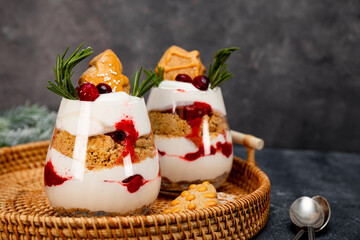Two glasses of Christmas dessert with gingerbread cookies, whipped cream and cranberries on grey background