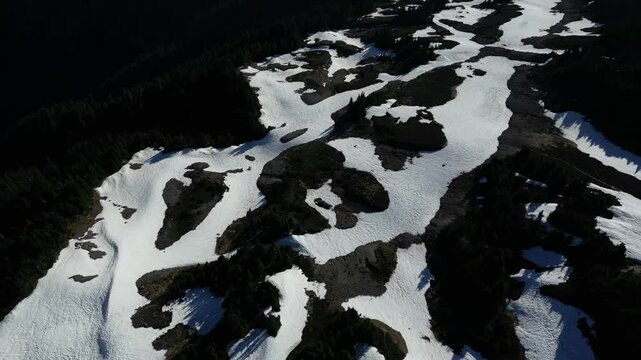 Drone footage looking down on a snowy mountain top. Patches of snow cover the dark landscape on a sunny, bluebird day. British Columbia, Canada.