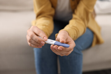 Woman holding pregnancy test on sofa indoors, closeup