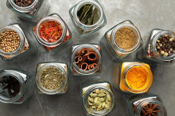 Different spices in glass jars on grey table, flat lay