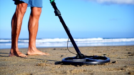 Metal detector coil and human feet on the beach. Close-up of the latest generation plate and the high-tech electronic apparatus that analyzes the wet sand