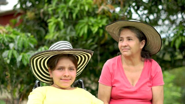 Young Woman in Wheelchair Wearing Colombian Hat Enjoying a Day Outdoors with Her Grandmother at a Farm